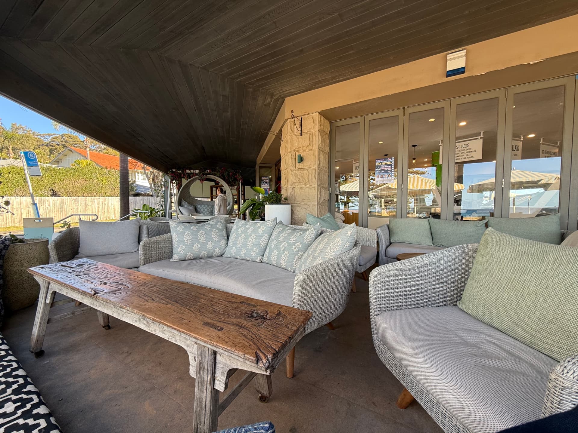 Wicker lounges with green cushions and a timber table on the cafe terrace